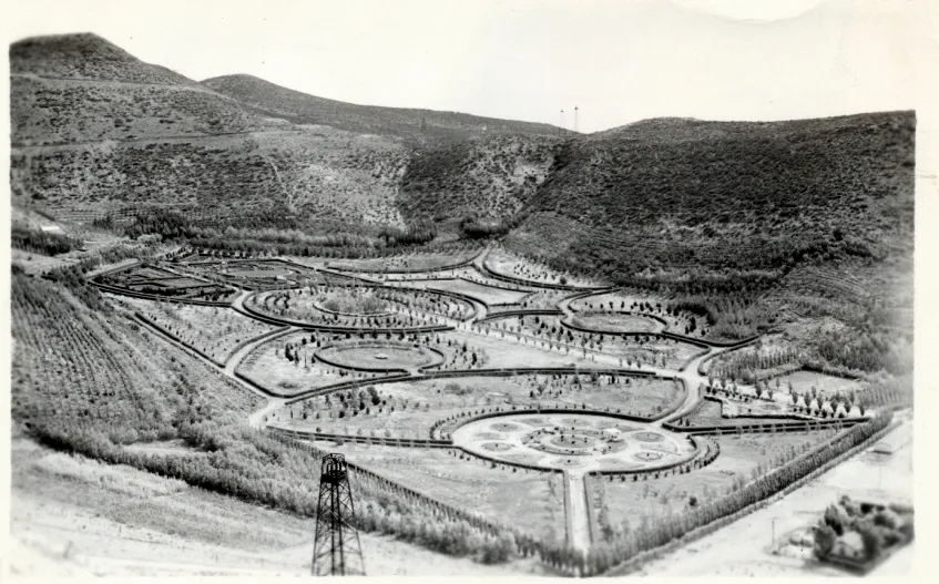 Foto de archivo del Parque Saavedra en sus comienzos: canteros y caminos en círculos en el fondo del valle, árboles jóvenes y una torre de perforación petrolera en primer plano