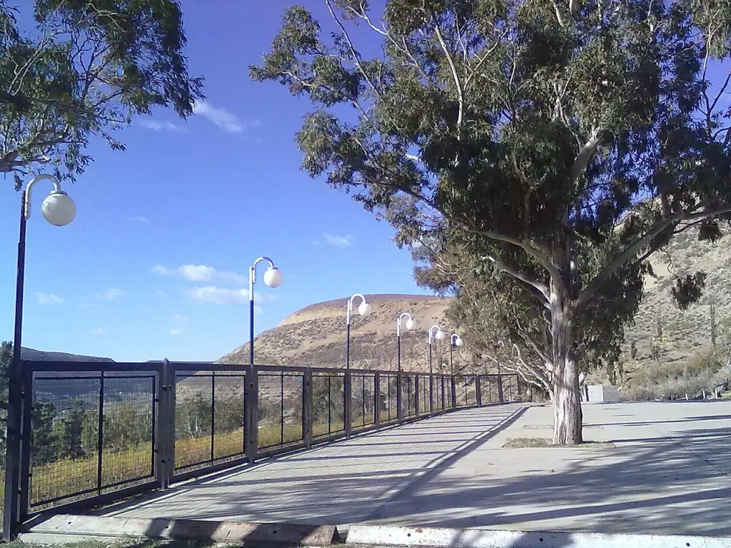 Un paseo del Parque Saavedra con faroles, baranda y eucaliptos, en lo alto, con el valle y los cerros detrás