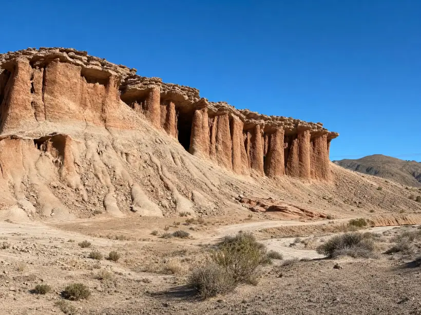 Pared de roca colorada erosionada en columnas en Rocas Coloradas, al norte de Comodoro Rivadavia, con una huella de tierra y arbustos de estepa al pie
